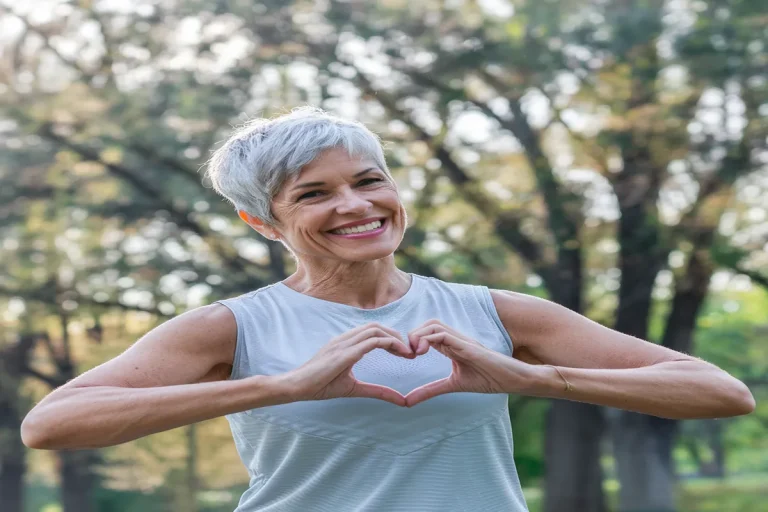 Mujer de mediana edad al aire libre formando un corazón con las manos, representando bienestar y consejos naturales para tratar el ojo seco